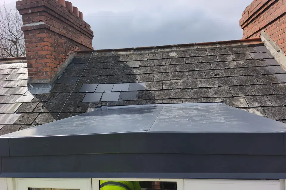 Flat roof on a rear extension below a slate roof and chimneys
