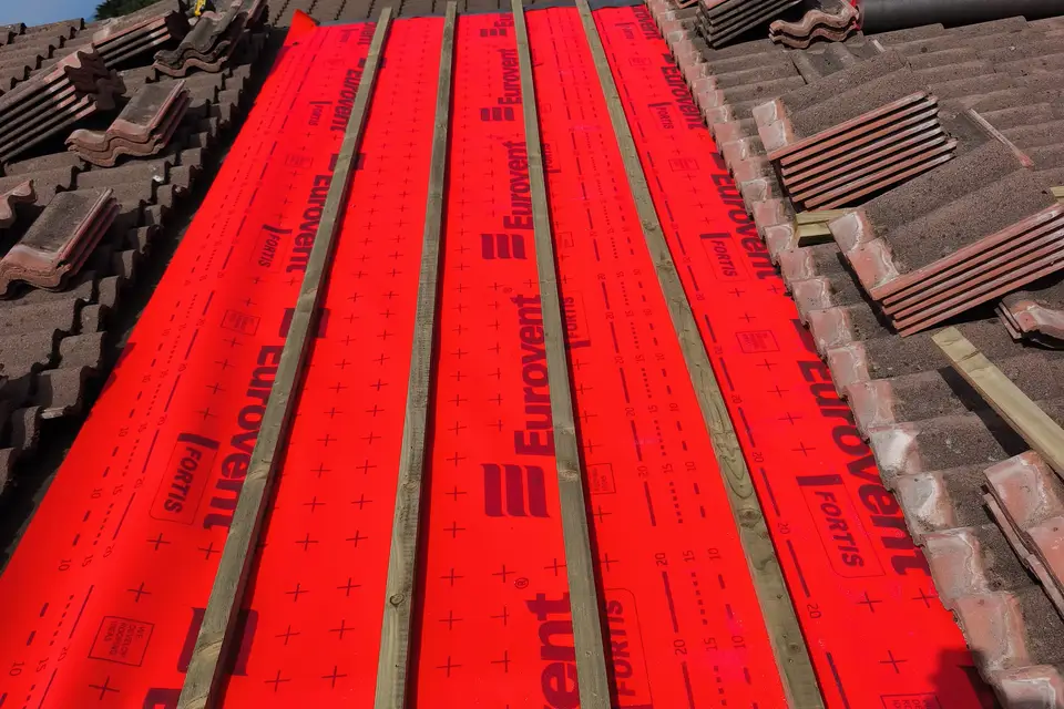 New breathable roof membrane and battens laid on a pitched roof, old tiles stacked to the side